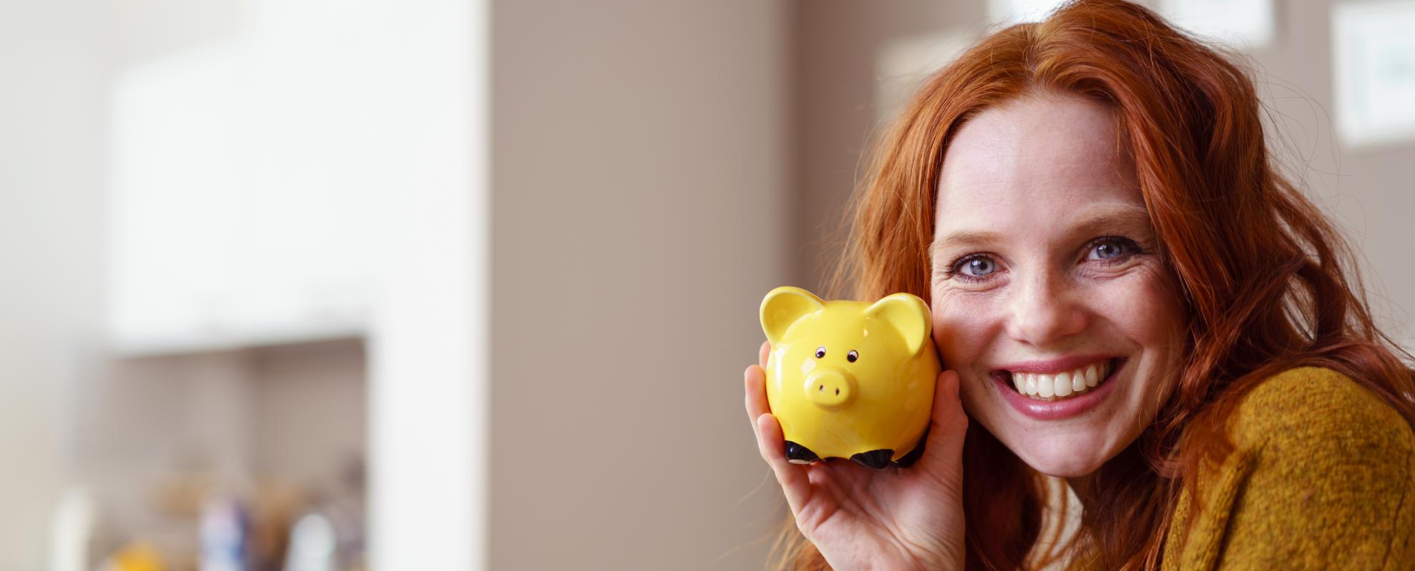 Lächelnde Frau hält ein Sparschwein in der Hand